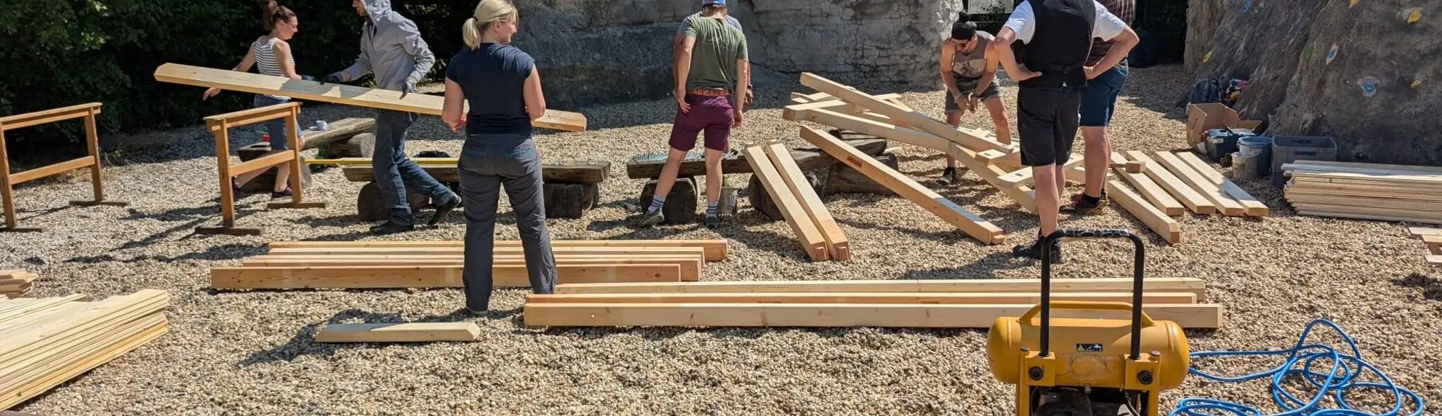 Mehre Personen sortieren die Bauteile aus Holz für eine der beiden Sitzgruppen. Im Hintergrund befindet sich der Braschelstein. | © Horst Jatzlauk