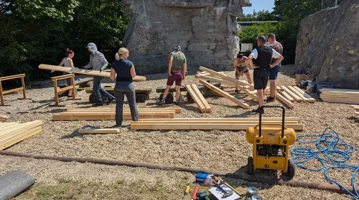 Mehre Personen sortieren die Bauteile aus Holz für eine der beiden Sitzgruppen. Im Hintergrund befindet sich der Braschelstein. | © Horst Jatzlauk