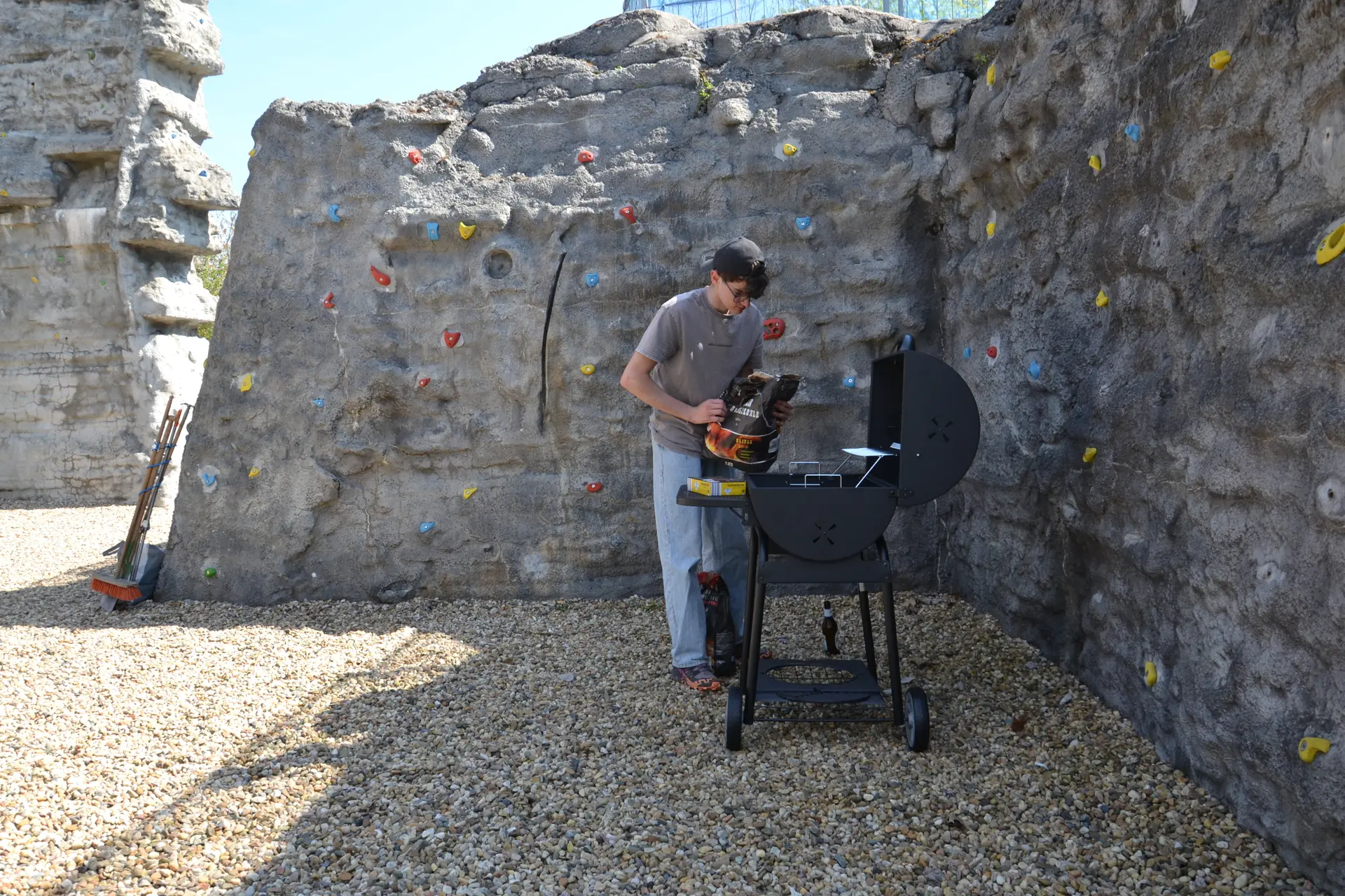 Eine Person kippt Holzkohle in den Grill; im Hintergrund die Boulderwand. | © 	 Theodor Kubusch